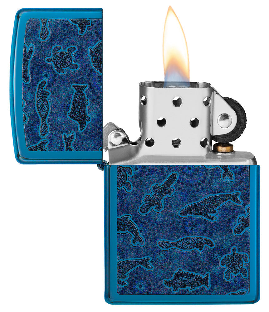 Zippo aansteker vooraanzicht geopend en aangestoken in hoogglans blauw met illustratie van zeedieren in de stijl van Aboriginal kunst.